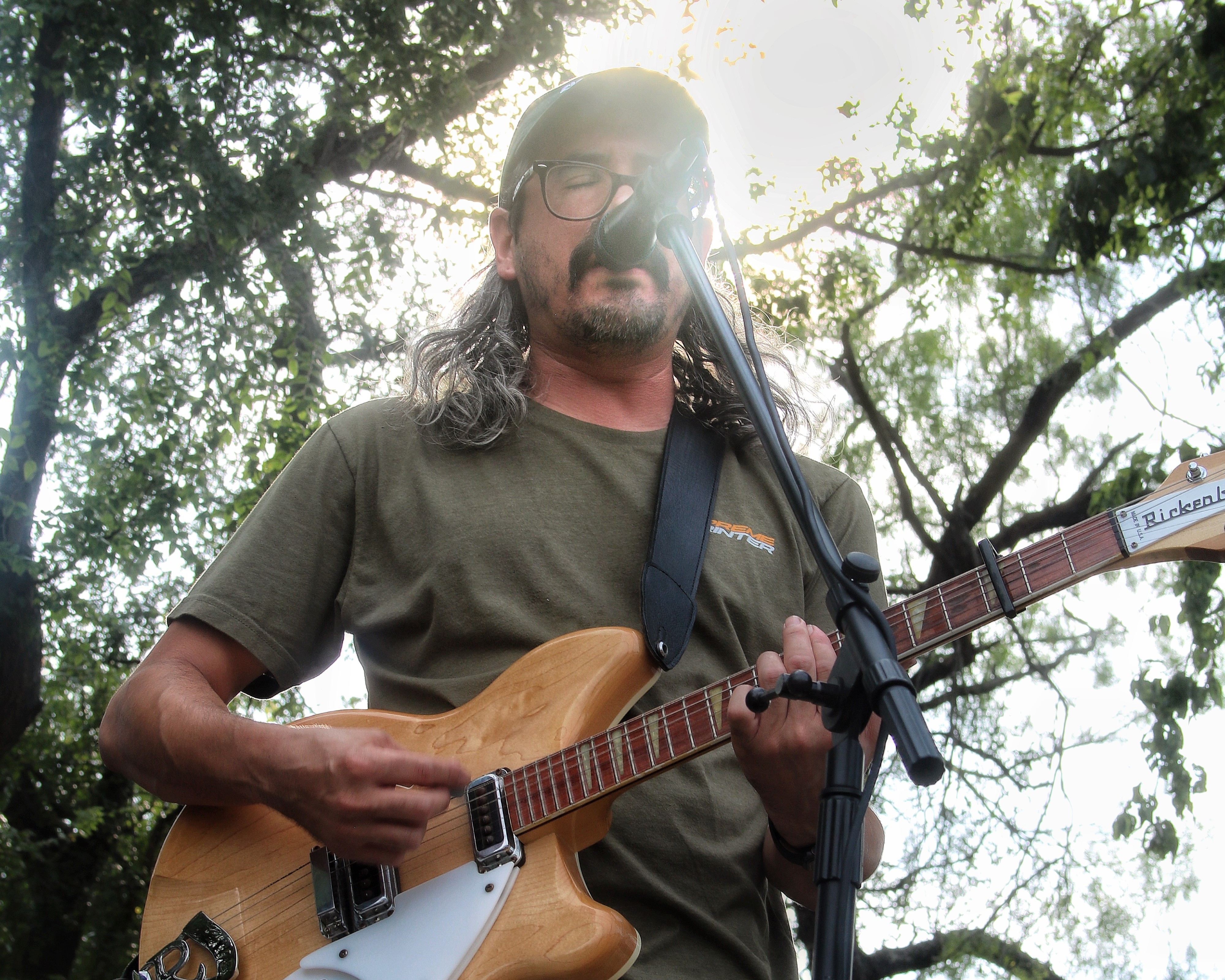 Photo of guy singing outside, into a mike while playing the guitar